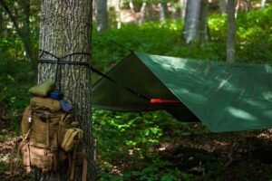 Vihreä riippumatto ja tarppi ripustettuna metsään, puuhun kiinnitettynä myös retkeilyreppu.