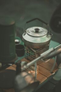 Metallinen teekannu keittää vettä risukeittimen päällä retkivarusteiden ympäröimänä. Retkikeitin sopii ulkoiluun ja eräkäyttöön.