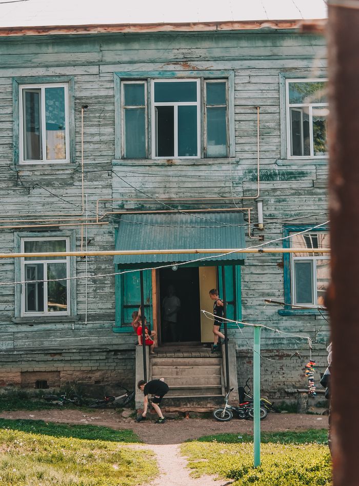 Children play around a rustic wooden house entrance, capturing a carefree summer day.