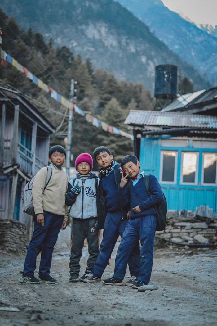 Four boys posing on a dirt road in a Himalayan village, showcasing cultural attire.