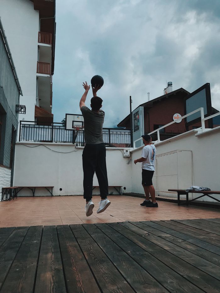 Two men playing basketball on a rooftop court under a cloudy sky, capturing a dynamic sports moment.
