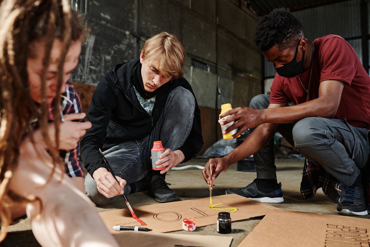Young adults painting signs in an industrial setting, engaged in creative expression.