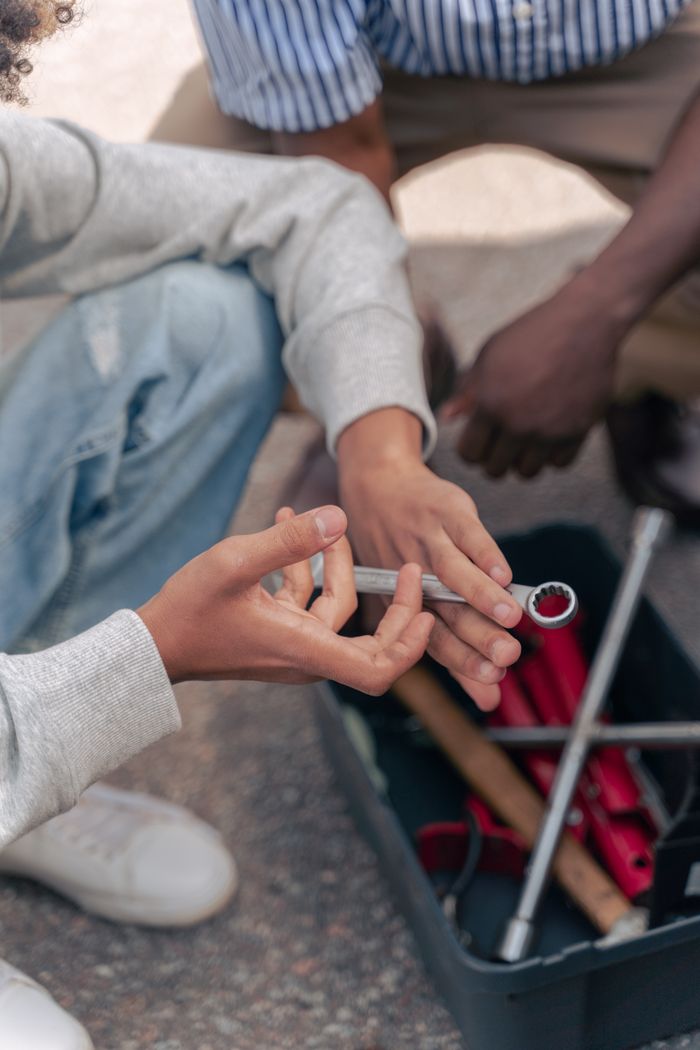 Close-up of hands exchanging a wrench outdoors, focusing on teamwork and learning.
